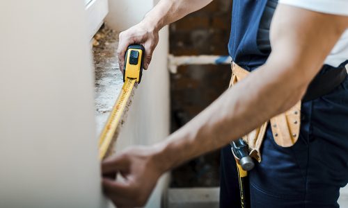 cropped view of handyman measuring wall with yellow measuring ta
